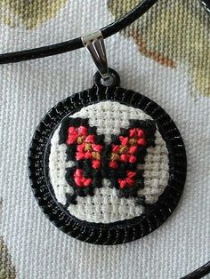 a black and white cross stitched necklace with red flowers on the inside of it