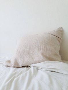 an unmade bed with white linens and a pillow on it's side