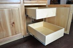 an open drawer in the middle of a kitchen with wood floors and cabinets behind it