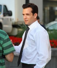 a man in a white shirt and black tie talking to another man on the street