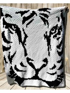 a crocheted blanket with a white tiger face on it, hanging from a wooden fence