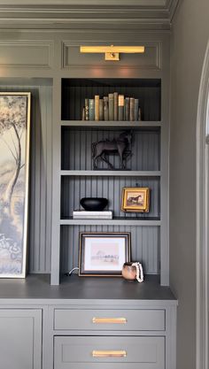 a book shelf with books and pictures on it in a room that has gray painted walls