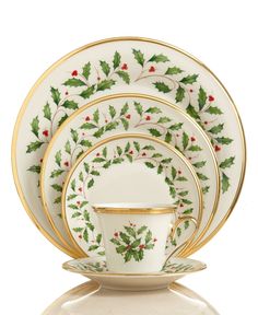 a white and gold christmas dinner set with holly designs on the front, two cups and saucers