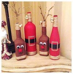 three wine bottles decorated to look like santa's stockings and reindeer noses, sitting on a mantle