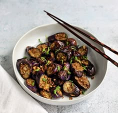 a white plate topped with cooked eggplant and chopsticks next to it