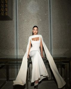 a woman sitting on top of a chair wearing a white dress and cape over her head