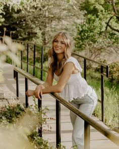 a woman leaning on a rail in front of trees