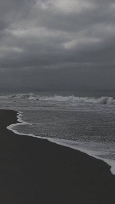 black sand beach with waves coming in to shore and dark clouds above the ocean on an overcast day