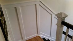 an empty staircase with white paneling and black handrails in a home's entryway