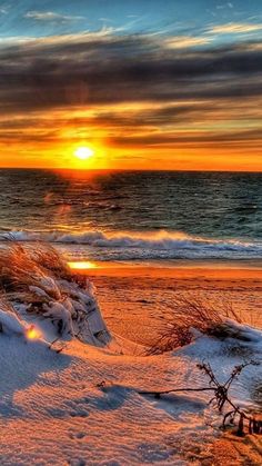 the sun is setting over the ocean on a beach covered in snow and sand with waves