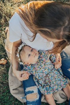 a woman holding a baby in her lap while sitting on the ground with other people