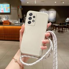 a person holding up a white phone case in a room with tables and couches