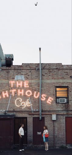 two people standing in front of a building with the words the lighthouse cafe painted on it