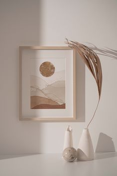 two white vases sitting on top of a table next to a framed art piece