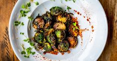 a white plate topped with brussel sprouts covered in seasoning on top of a wooden table