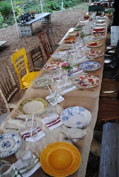 a long table is set up with plates and glasses for an outdoor dinner or party