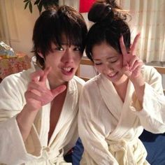 two people in robes making the peace sign with their hands while sitting on a bed