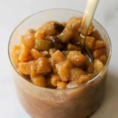 a glass bowl filled with food on top of a white table next to a spoon