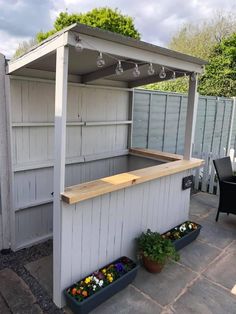 an outdoor bar with potted plants on the side and a table in front of it