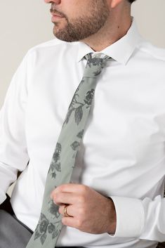 a man wearing a white shirt and gray tie with flowers on it, holding his hands in his pockets