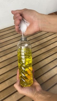 a hand holding a bottle filled with oil on top of a wooden table next to another hand