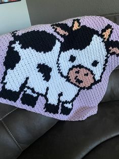 a crocheted cow blanket sitting on top of a black leather couch next to a wall