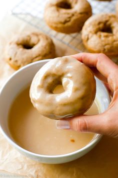 a person holding a donut over a bowl of doughnuts