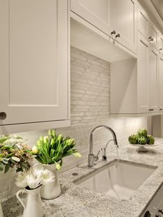 a kitchen with marble counter tops and white cabinets, along with two vases filled with flowers