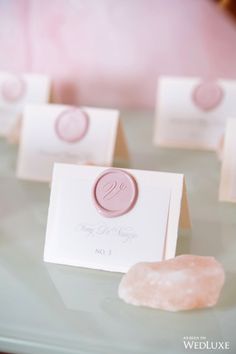 pink and white place cards are sitting on a glass table with small rocks in front of them