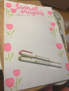 a notepad with two pens on top of it and some pink flowers around it