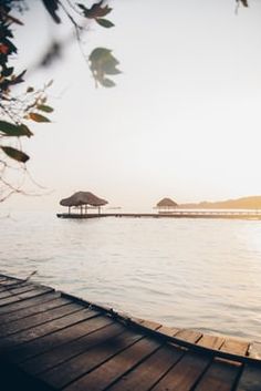 the sun is setting over the water and some huts are in the distance on the dock