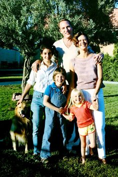 a family posing for a photo in the grass with a dog and tree behind them