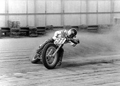 a man riding on the back of a motorcycle down a dirt road in front of a building