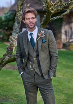 a man wearing a suit and tie standing in front of a tree with his hands in his pockets