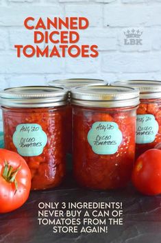 three jars filled with canned tomatoes sitting on top of a table next to two tomatoes