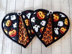 three black and orange halloween heart shaped oven mitts with pumpkins, ghostes and jack - o'- lanterns on them