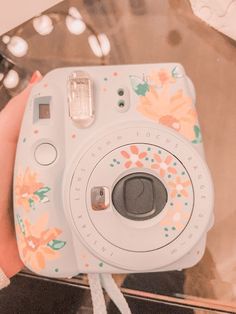 a person holding a white camera in their left hand and wearing a flowered wristband