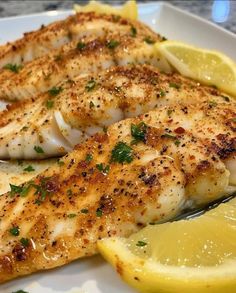 two fish fillets with lemon wedges on a white plate