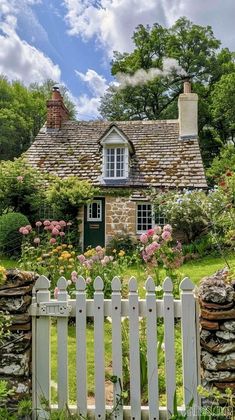 a white picket fence in front of a stone house with flowers growing on the lawn