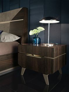 a night stand with a lamp on it next to a bed