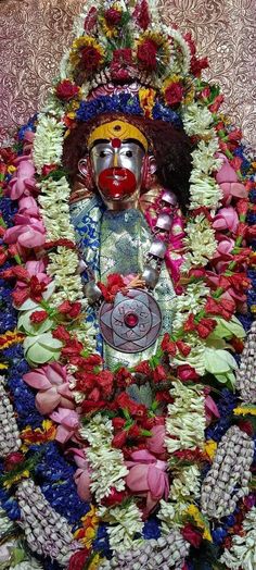 a statue is surrounded by flowers and other things in the background, with a red clown's face painted on it