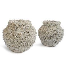 two white vases sitting next to each other on a white surface and one is made out of rocks