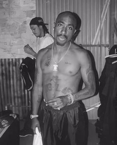 a black and white photo of a man with tattoos on his chest standing next to luggage