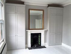 an empty room with white painted walls and a large mirror on the fireplace mantel