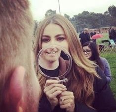 a woman looking through a magnifying glass at another person in the grass with other people behind her