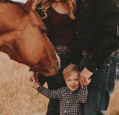 a young boy is holding the hand of his mother and father as they stand in front of a horse