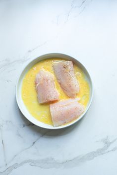 two pieces of raw fish in a bowl on a marble counter top with yellow liquid