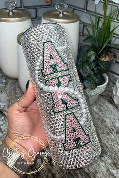 a person holding up a case with letters on it and pearls around the edges, in front of a potted plant