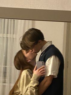 a young man and woman are kissing in front of a mirror with curtains behind them