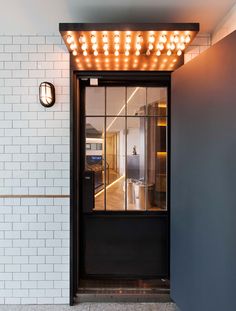 an open door with lights on the side of it in front of a white brick wall